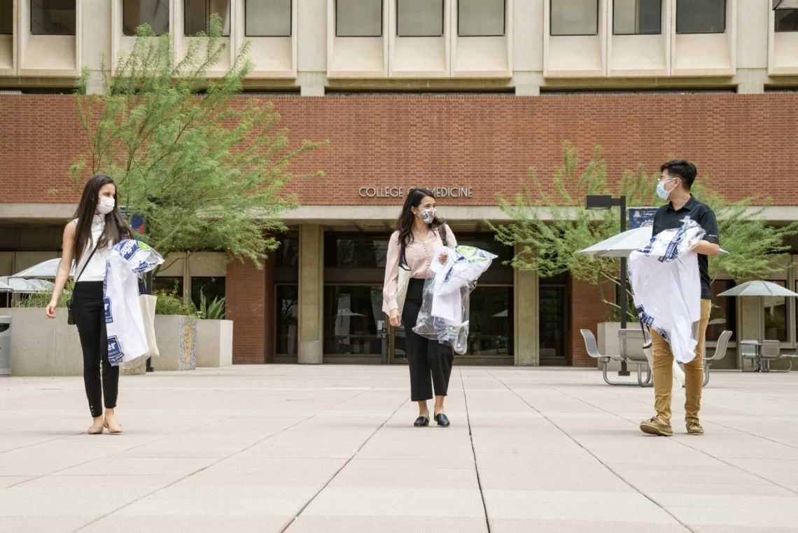 White coats in hand, three new members of the Class of 2024 leave the College of Medicine – Tucson building. From left: Lupita Molina, Julia Alvarenga Couto and Lawrence Sun.