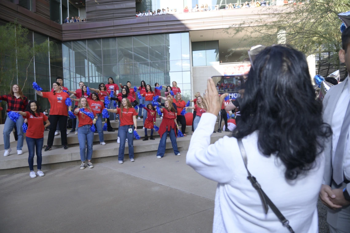 Back of a woman witih dark brown hair taking a photo of dancers performing on a small stage.