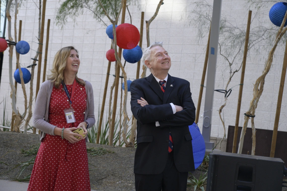 A middle-aged woman with blonde hair stands next to an older man with gray hair. Both are looking up to the right and smiling. 