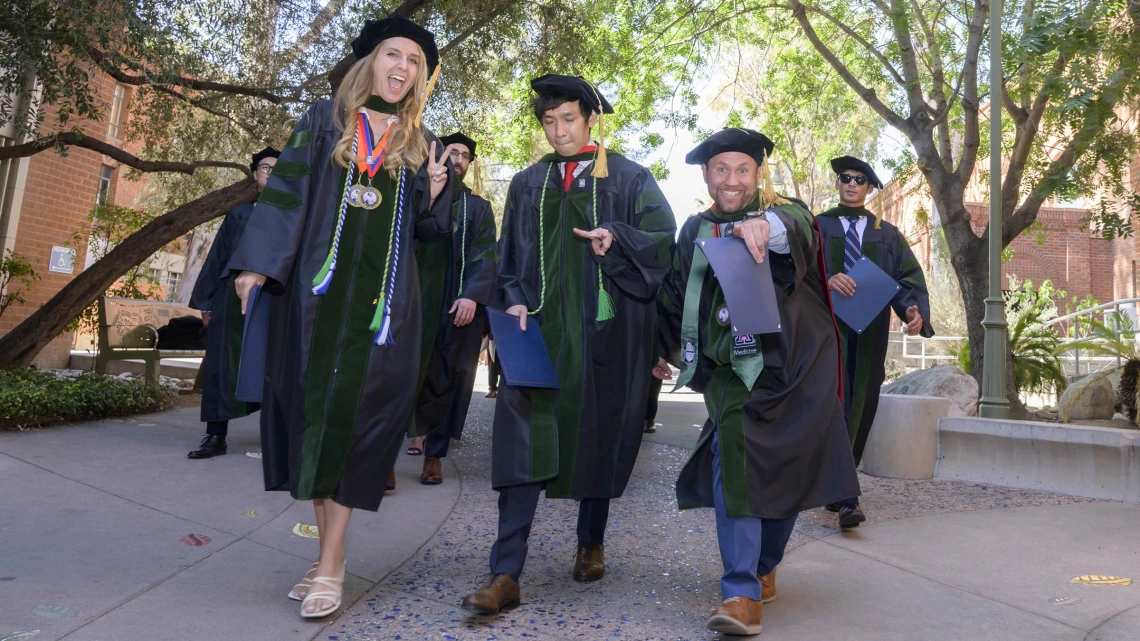 Several pharmacy students in graduation regalia smile as they walk outside after their graduation ceremony.