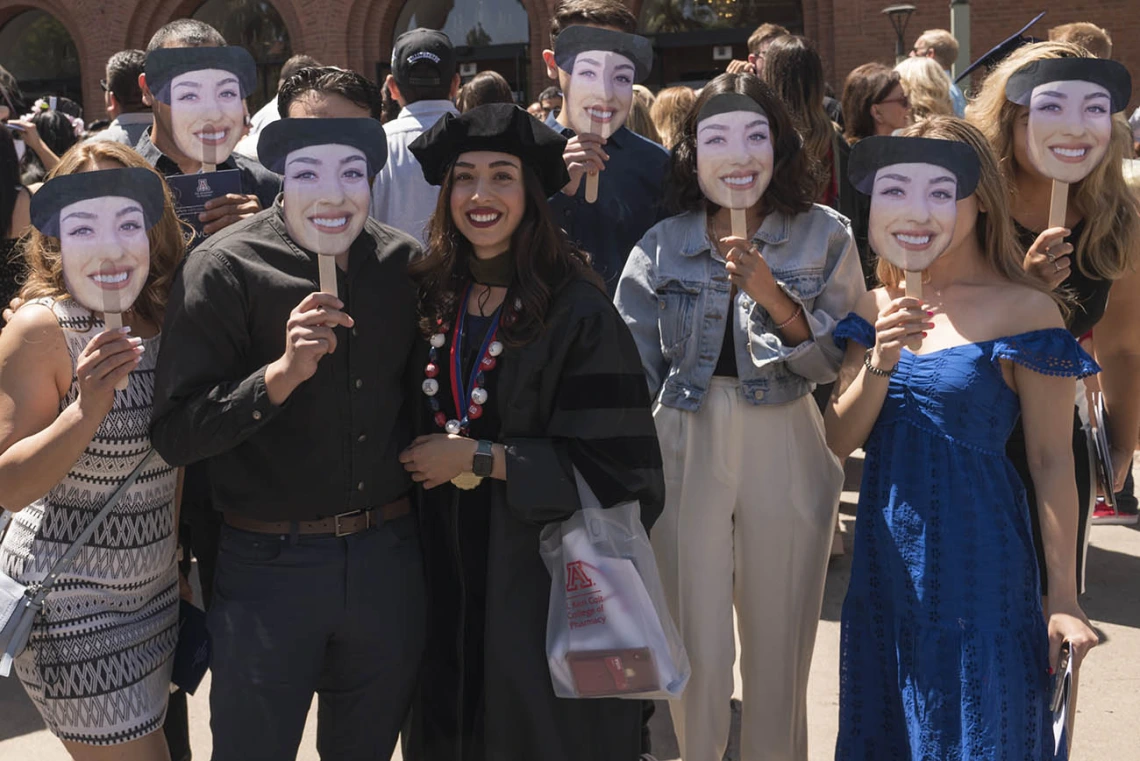 Daisy Arellano, PharmD, poses for a photo with her family – who all hold up photos of her face – after the R. Ken Coit College of Pharmacy 2022 spring convocation at Centennial Hall.  