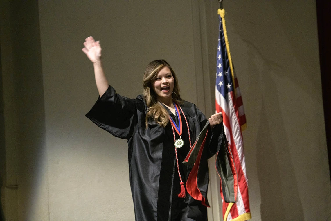 Diana Pham, PharmD, waves to the audience as she walks across the stage to be hooded during the R. Ken Coit College of Pharmacy 2022 spring convocation at Centennial Hall. 