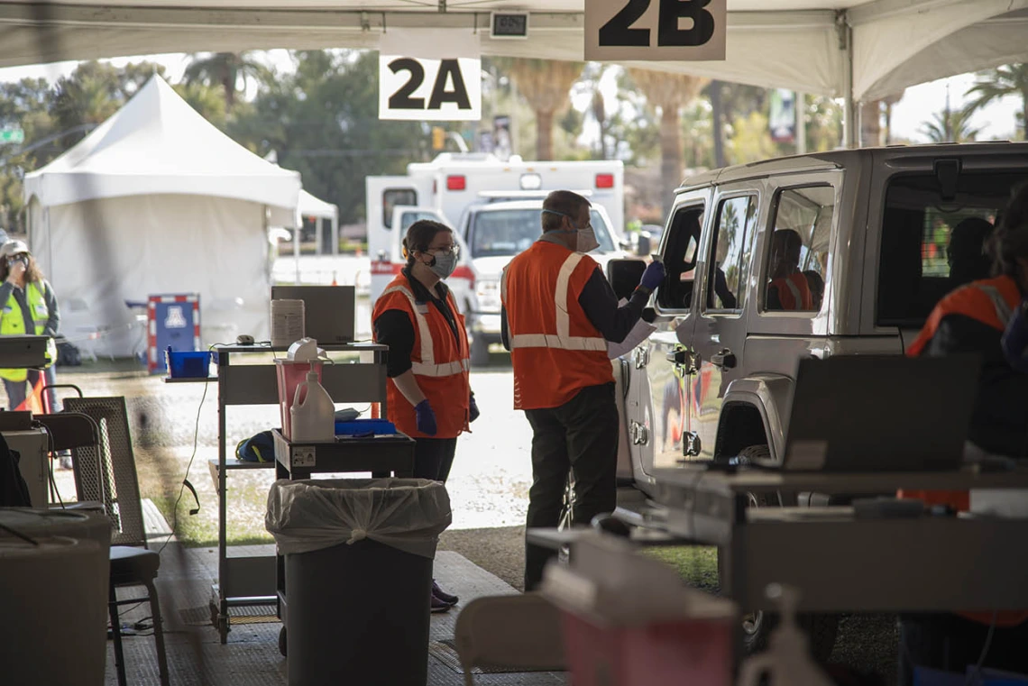 Leslie Farland, ScD, assistant professor at the UArizona Mel and Enid Zuckerman College of Public Health, volunteers as a scribe (left), while College of Pharmacy professor Michael Katz, PharmD, talks to a patient before administering the COVID-19 vaccine. 