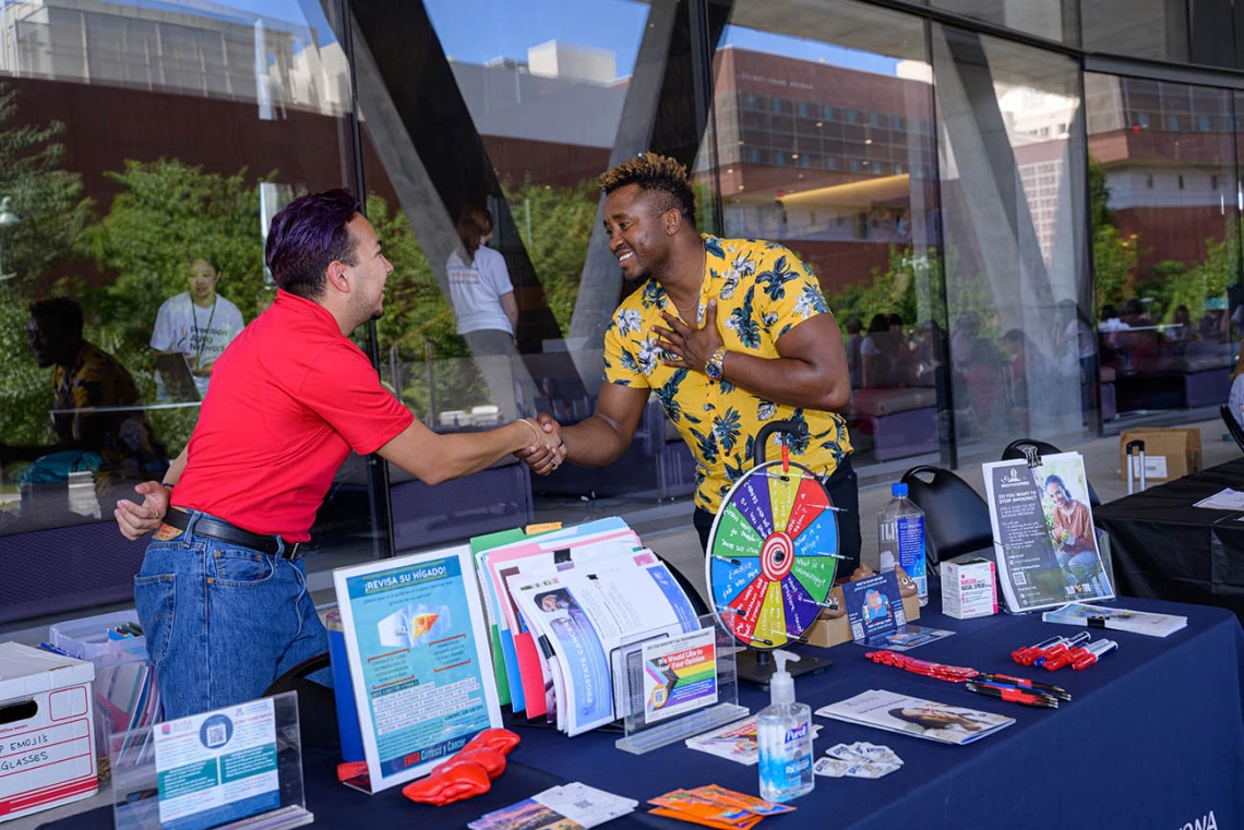 (From left) Juan Contreras II, a research program administrator, greets Tony Philippe, LL.B, a health educator, as they begin their volunteer shift at the University of Arizona Cancer Center information table at the Feast for Your Brain event.