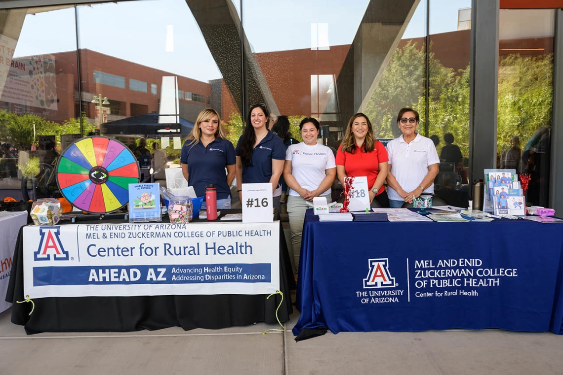 Five women stand behind information tables with banners for the UArizona Center for Rural Health. 