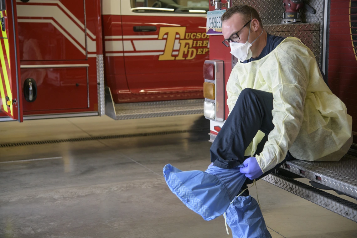 Tucson Fire Department’s Taylor Parrish puts on a protective gown and boot coverings to prevent spread of disease before entering the home a possible COVID-19 patient.