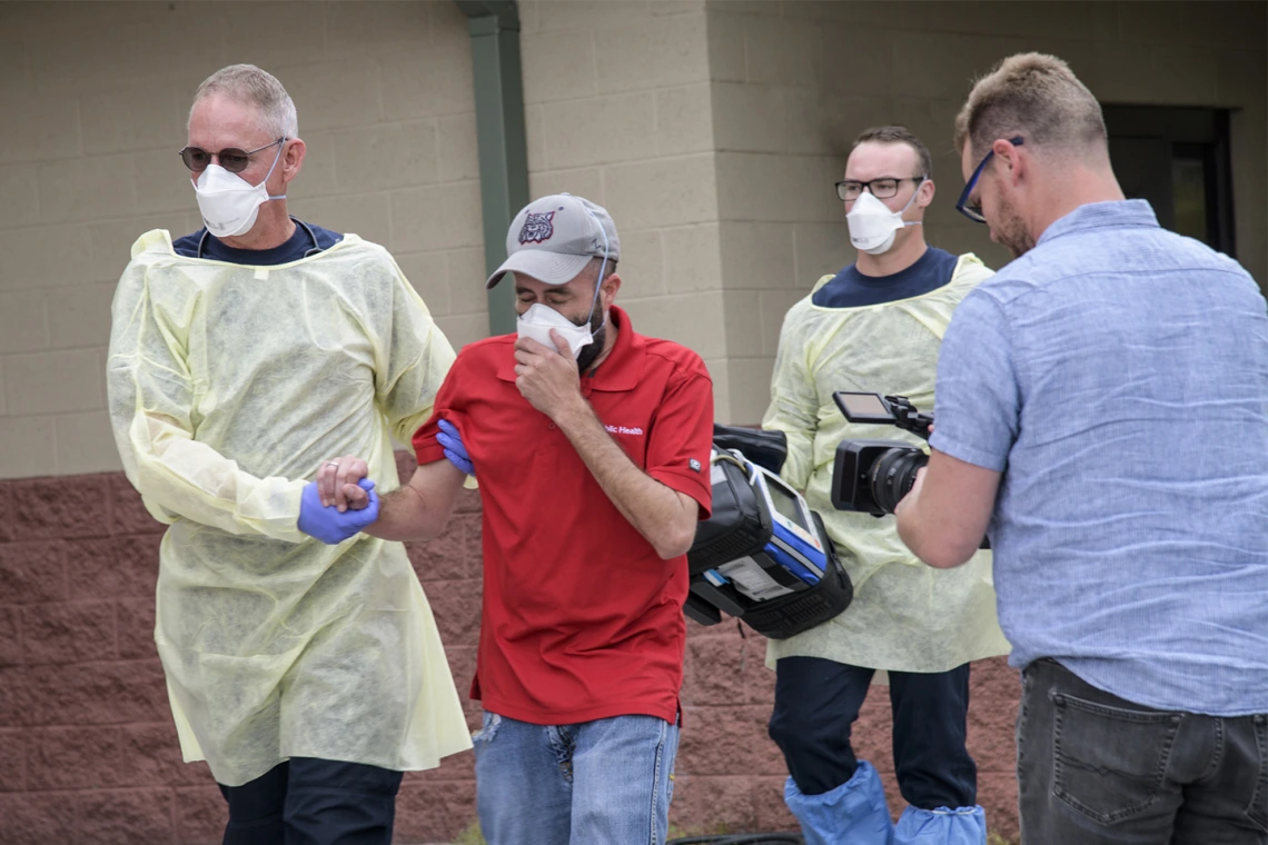 Erich Healy, right, films as Tucson Fire Department’s Chris LaFave, left, helps guide Jonathan Sexton, PhD, who is playing a possible COVID-19 patient in a training video, into an ambulance.