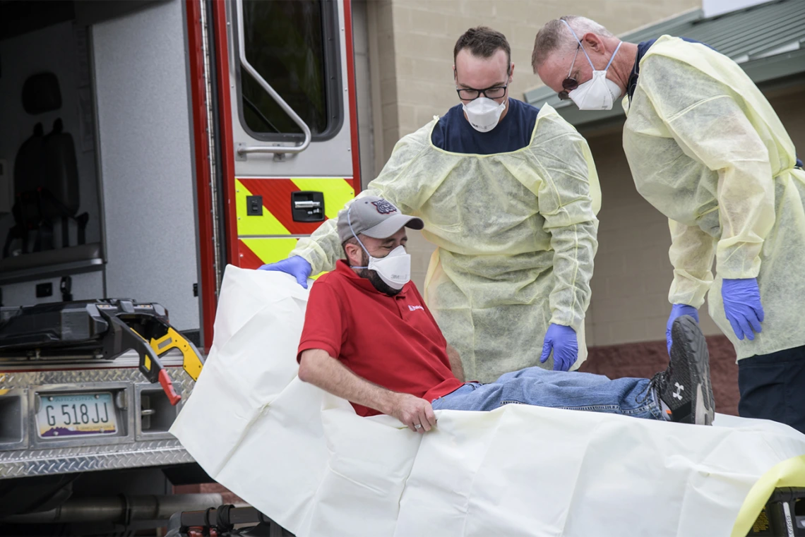 Firefighters Taylor Parish and Chris LaFave wrap Jonathan Sexton, PhD, in a protective barrier to demonstrate how to prevent the spread of a virus during an ambulance trip to the hospital. Sexton is a researcher in the Mel and Enid Zuckerman College of Public Health, participating in a training video in March to help first responders learn protective measures for possible COVID-19 patients.