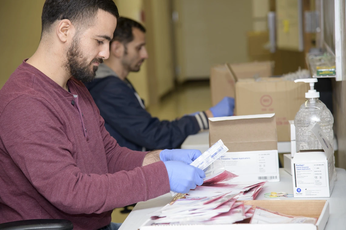 Biorepository laboratory techs Ayman Sam (left) and Brandon Jernigan (right) complete the final step to assemble the COVID-19 sample collection kit.