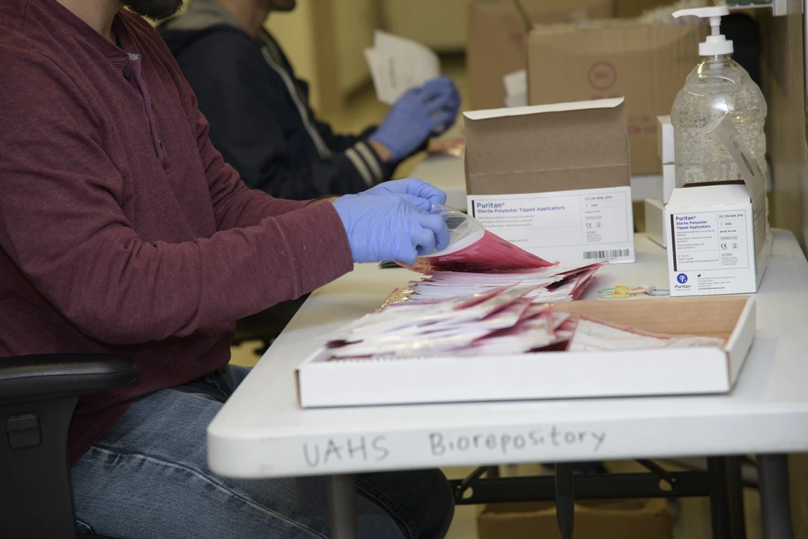 Biorepository laboratory technicians Ayman Sam (left) and Brandon Jernigan (right) complete the final step to assemble a COVID-19 sample collection kit.