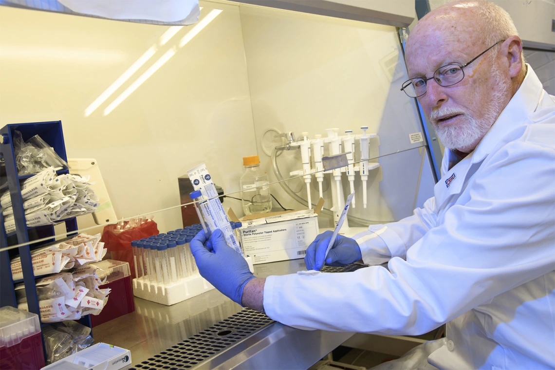 David T. Harris, PhD, holds up items from a sample collection kit under a serial hood. 