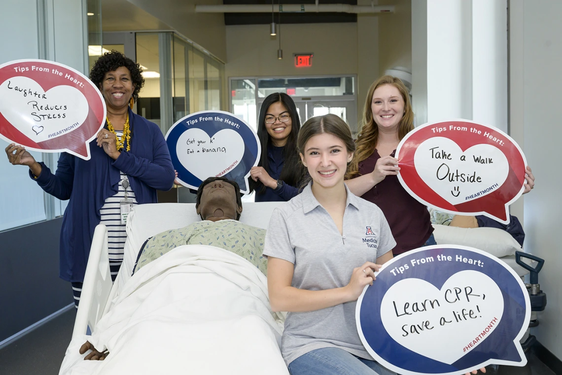 4 women stand around a patient manikin holding heart posters