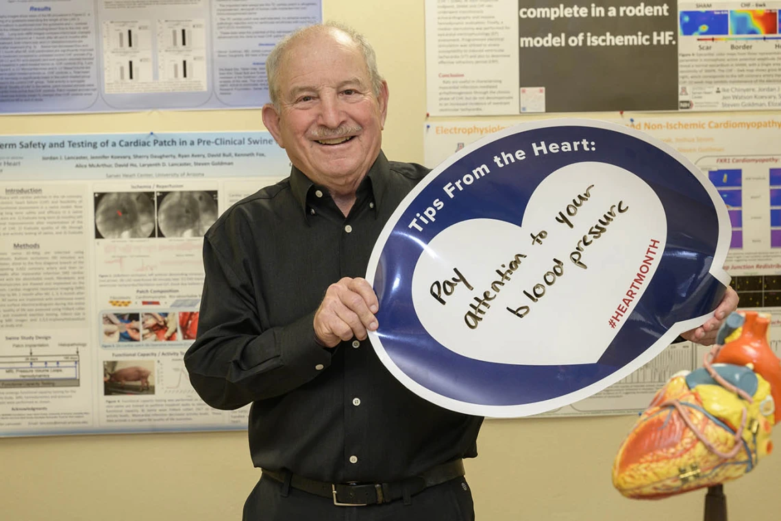 Older, balding man in black shirt holds a heart poster that says Pay attention to your blood pressure. 