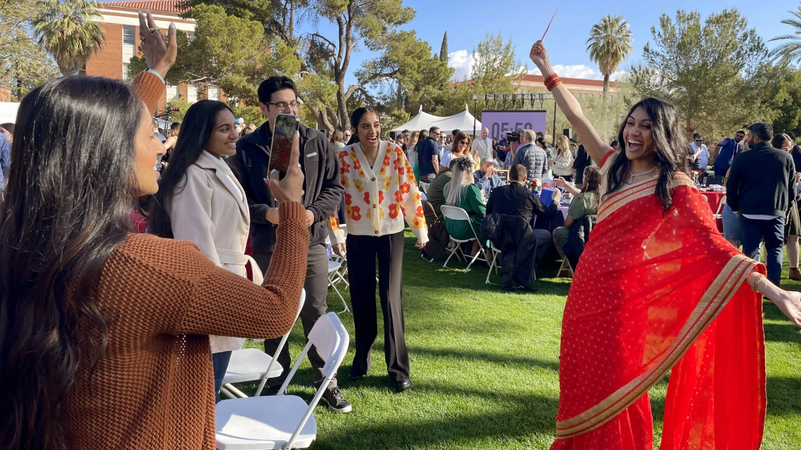 Woman in red sari poses with arms out while family members take photos.