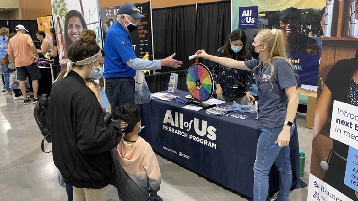 Marissa McLelland (right) an engagement coordinator with All of Us UArizona – Banner, talks with people interested in the program while she hands out information and branded hand sanitizer. 