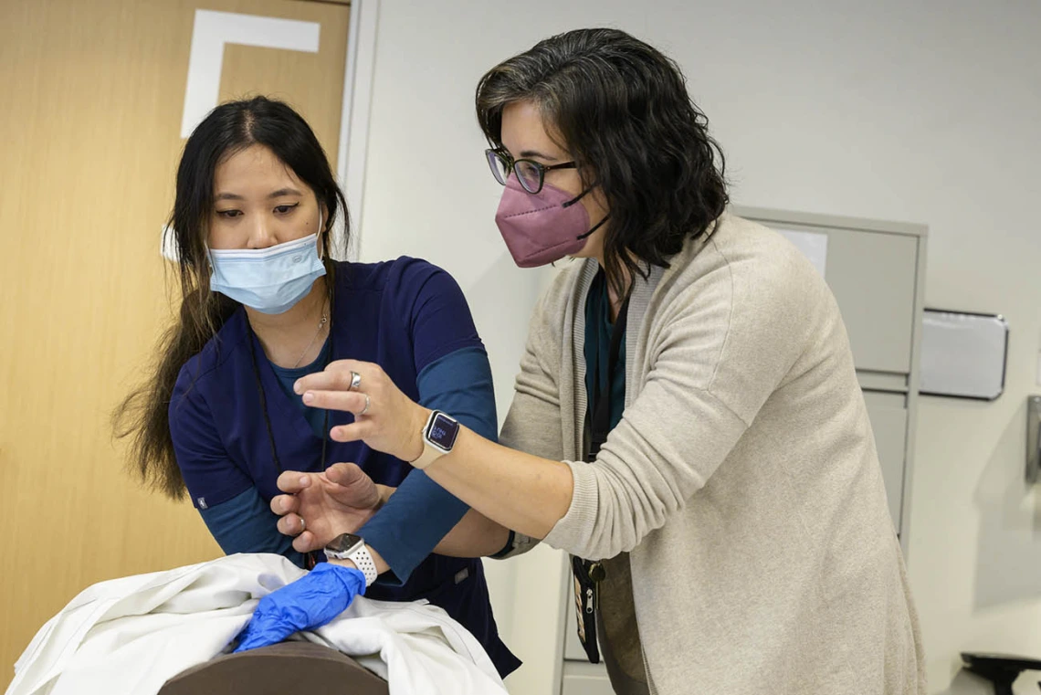 A Doctor of Nursing Practice nurse-midwifery student watches as an instructor demonstrates fundal massage on a manikin for during a clinical immersion session.