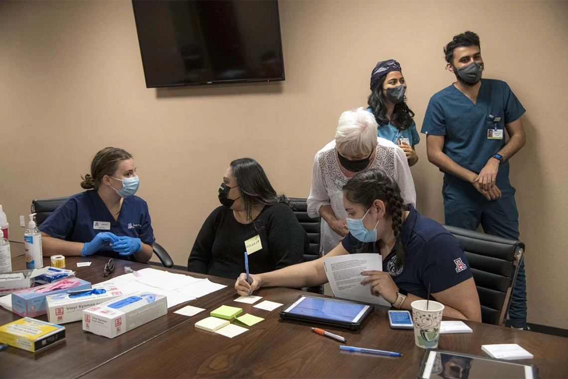 Public Health student and scribe Diana Grijalva (on right in front) writes as College of Nursing preceptor Nancy McGuckin, RN, MSN, MPH (standing with white hair) advises her. On the left, Nursing student Valerie Pedersen prepares to vaccinate a patient (center). Behind (on right) are College of Medicine senior students Maya Sarihan and Abdullah Aleem, who also participated as vaccinators.