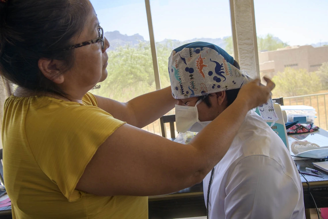 Navajo seamstress Theresa Hatathlie-Delmar checks the fit of a surgical cap on College of Medicine – Tucson student Aaron Bia.