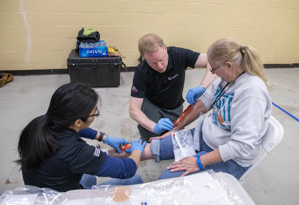 Merryl Lopido, simulation operations specialist for ASTEC, and David Biffar, ASTEC’s assistant director of operations, use special-effects makeup to simulate traumatic injuries on volunteer Helen Ward’s leg. Many volunteers received simulated wounds with fake blood or embedded debris.