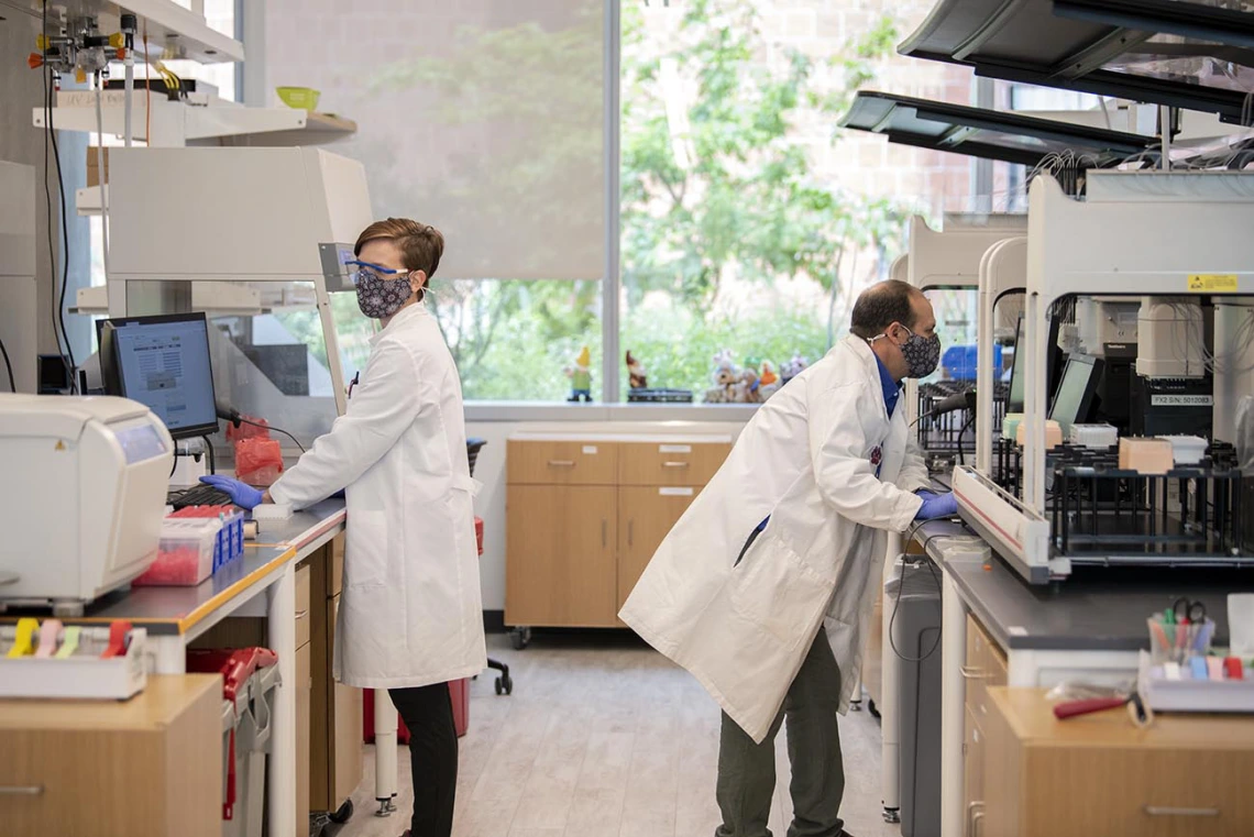 Barbara Fransway (left), manager of University of Arizona Genetics Core Research Services, transfers blood serum to testing plates as Matthew Kaplan, manager for University of Arizona Functional Genomics Core, evaluates the Biomek robot prior to performing antibody testing.