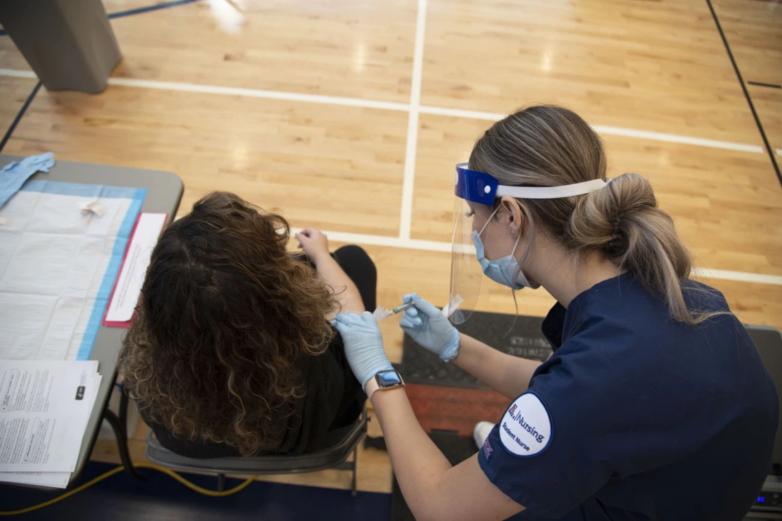 After taking a COVID-19 antigen test, a student receives a flu shot from College of Nursing student Genevieve Veneziale, who says the secret to giving a good shot is “remaining calm and talking to your patient, making sure they stay calm and making sure they’re relaxed.”