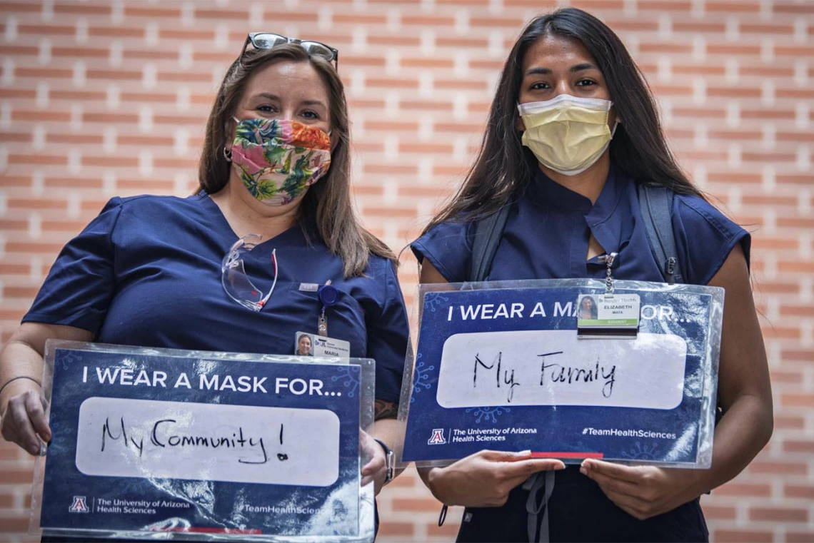 Maria Williams and Elizabeth Mata, third-year College of Medicine – Tucson students, share their signs. Williams wears a mask for her community and Mata wears a mask for her family. 