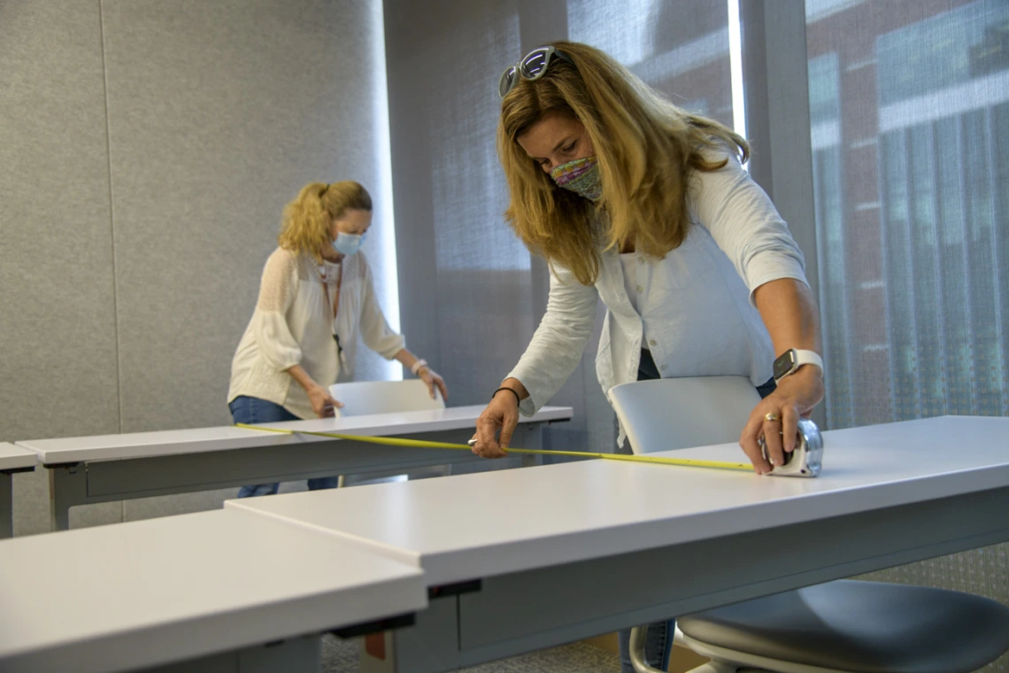 Mary Matthews, left, and Angie Souza, right, of Health Sciences Planning and Facilities, measure the distance between desks in the Health Sciences Innovation Building to design new seating arrangements to ensure people stay six feet apart.