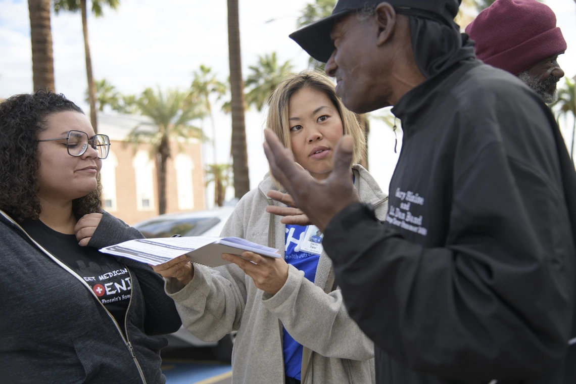 Street Medicine Phoenix volunteers help a patient complete an assessment form outside of Grace Lutheran Church.