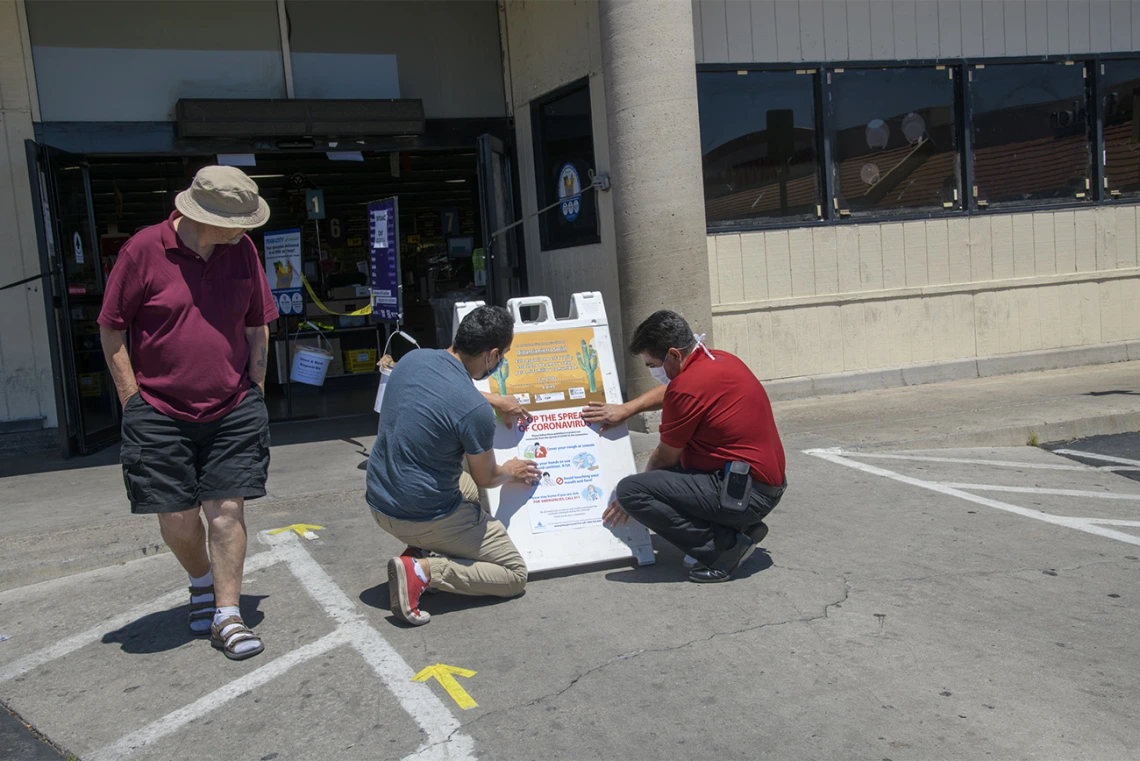 A customer walks by as fourth-year medical student Ricardo Reyes and Ramon Lopez, store manager of the Food City on West Ajo Way in Tucson, hang a social distancing poster at the entrance of the store. Reyes and his peers in the College of Medicine – Tucson designed many of the posters as outreach about ways to practice health precautions for Spanish-speaking communities in Arizona.