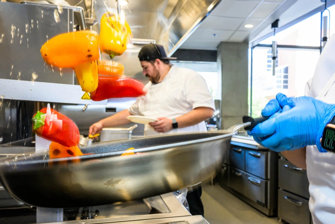 A skillet with colorful bell peppers tosses them in the air over a stove top. 