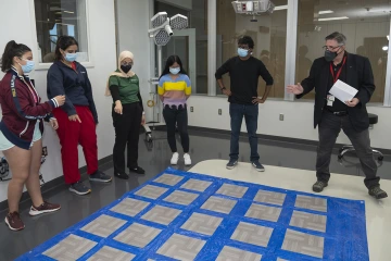 (From left to right): Hannah Rosen, Nadja Jones, Diyana Ahmad, Lyr Cerilla and Aryan Eksambe listen to Allan J. Hamilton, MD, FACS, explain the basic concepts and rules of the "Toxic Tile" game. 