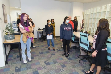 Several people stand around a common area in an office with a glass brick wall. 