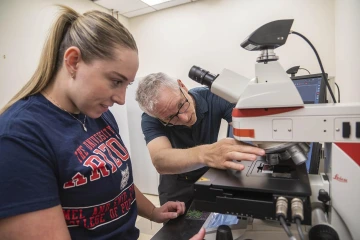 man adjusting a microscope with a female student observing