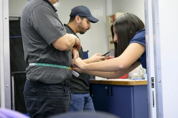 Sheila Soto has a tape measure wrapped around a man’s waist. 