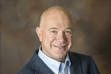 Mostly bald man with a pleasant smile wearing a blue collared shirt. 