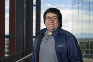 Lucas Grijalva, wearing an ASTEC jacket, stands outside on a balcony, smiling.