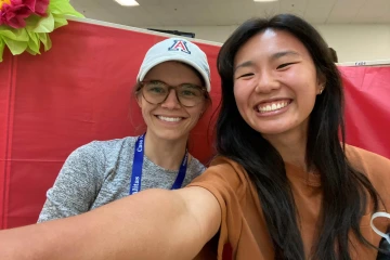 Selfie of Lauren Melcher, wearing a white University of Arizona ballcap, and Sarah Brock in front of a red backdrop