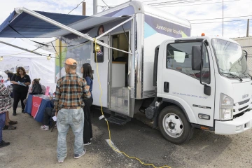 Public health workers in scrubs stand around an information table set up outside a parked mobile health unit truck.