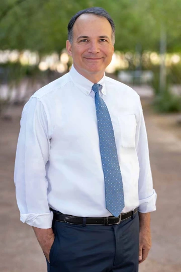 A man wearing a white shirt and blue tie stands outside.