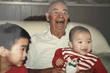 An older adult sits in a living room chair with two young children. 