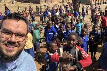 Onicio Leal is in the foreground in a selfie with a crowd of people, mostly children. 