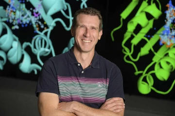 A portrait of Travis Wheeler, PhD, in front of brightly colored designs