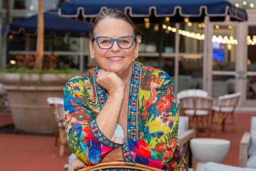 Portrait of Lorre Laws sitting at an outdoor cafe smiling. 