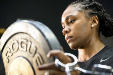 Close-up photo of the U of A’s Brena Andrews sliding a plate onto a barbell. 