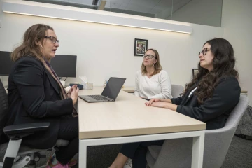 Chris Stallman, MLS, MS, Valerie Schaibley, PhD, and Hope Wollen are seated at a desk and talking