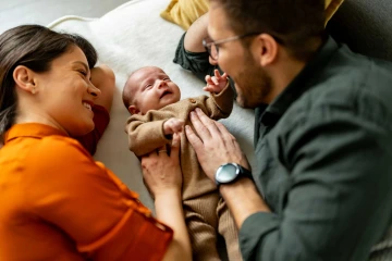 A mother and father playing with a baby lying on its back