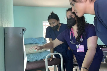 A female physician (center) trains medical students standing to the left and right of her.