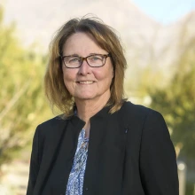 Portrait of Ann Cress, a white woman with shoulder-length light brown hair, wearing a dark blazer and glasses.