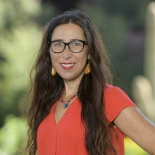 Portrait of Seephanie Russo Carroll, a Native American woman with long dark hair, wearing a red blouse and smiling.