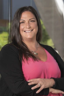 Smiling woman with dark brown hair wearing a pink top and a black cardigan